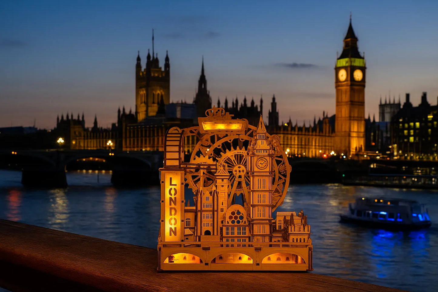 Maquette en bois illuminée représentant les monuments de Londres, posée sur une rambarde au bord de la Tamise avec Big Ben et le Palais de Westminster en arrière-plan au crépuscule.