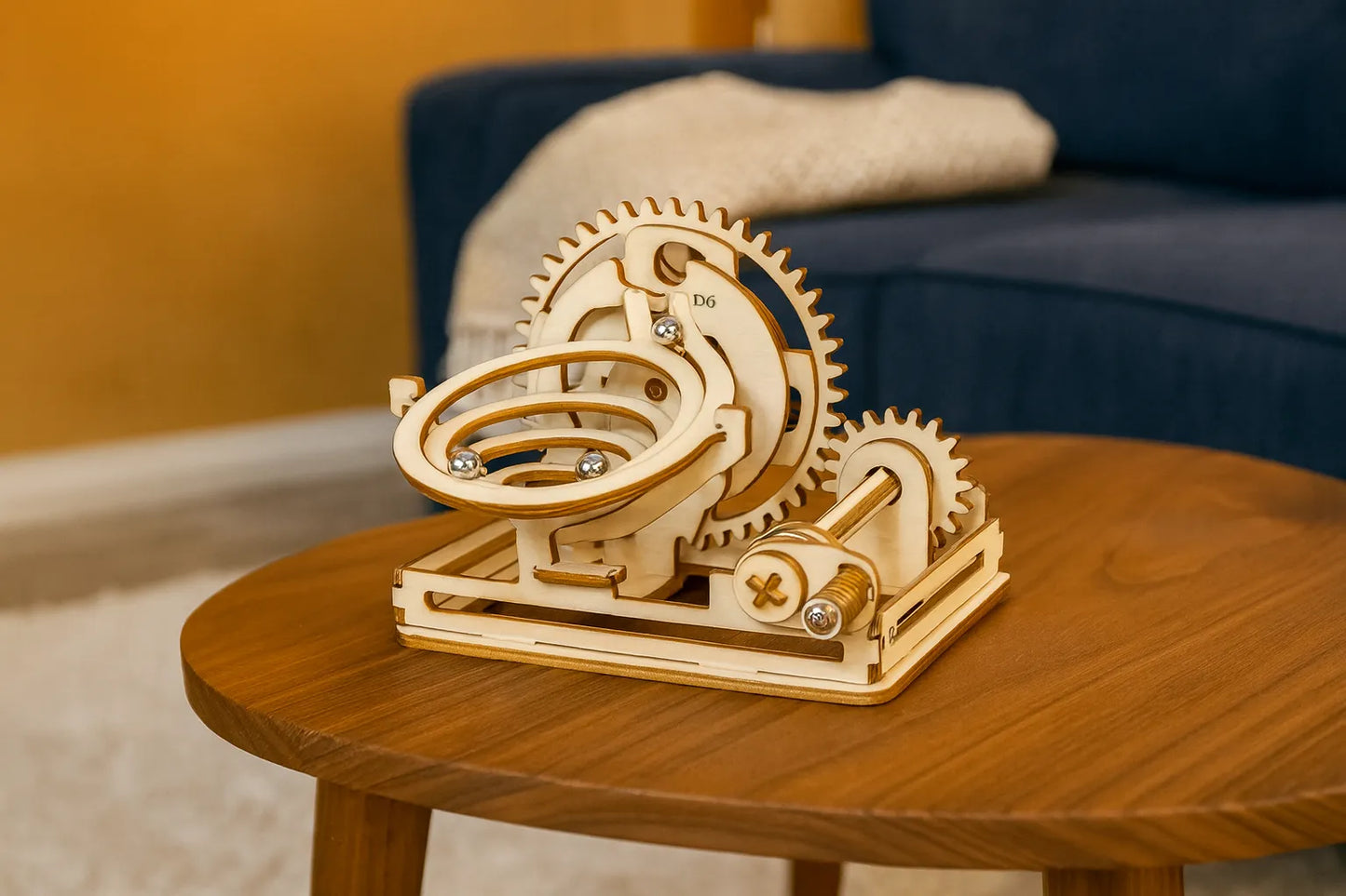 Maquette en bois d’une spirale de billes, avec engrenages circulaires et billes métalliques argentées, présentée sur une table basse en bois clair dans un salon.