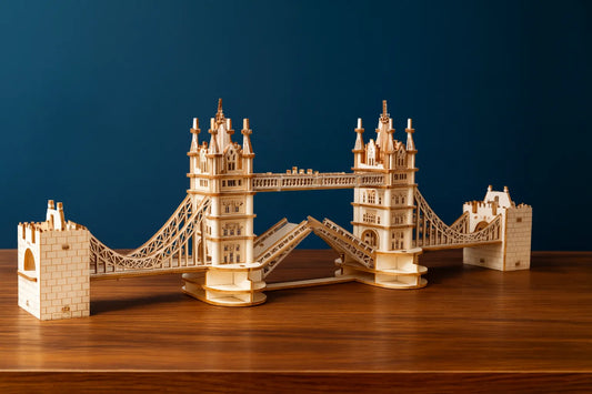Maquette en bois du Tower Bridge de Londres, posée sur une table en bois devant un fond bleu foncé.