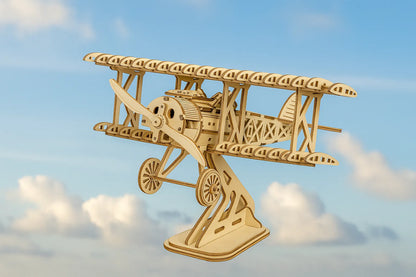 Maquette en bois d’un avion biplan vintage avec hélice et structure ajourée, posée sur un support et survolant un ciel clair aux nuages légers.