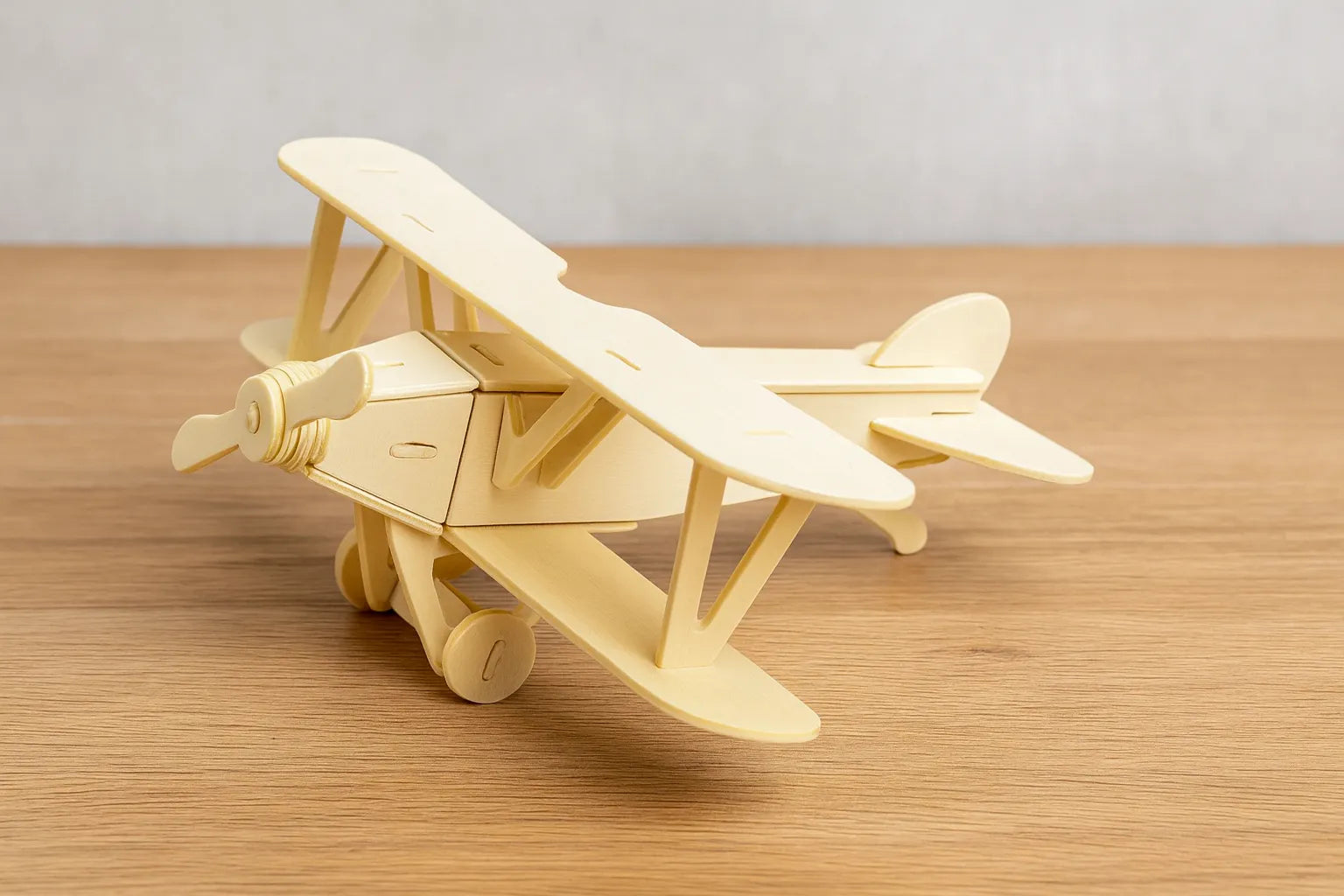Maquette en bois d’un avion biplan beige, posée sur une table en bois devant un mur gris clair.
