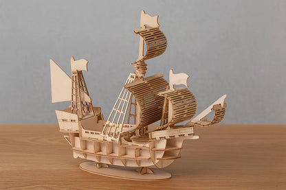 Maquette en bois d’un bateau pirate avec voiles déployées posé sur une table en bois devant un mur gris clair.