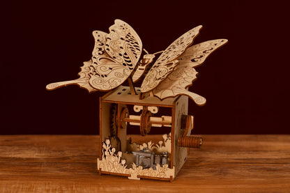 Maquette en bois artisanale de boîte à musique papillon, ornée de détails floraux gravés, fond rouge chaleureux.