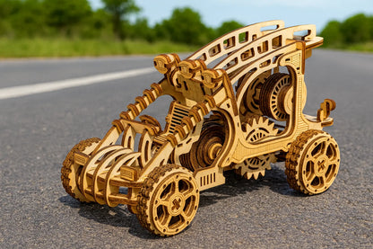 Maquette en bois d’un buggy mécanique, aux grandes roues crantées et aux engrenages apparents, exposée sur une route ensoleillée.