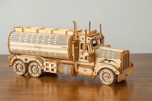 Maquette en bois d’un camion-citerne américain, finement gravée et posée sur une table en bois devant un mur gris clair.