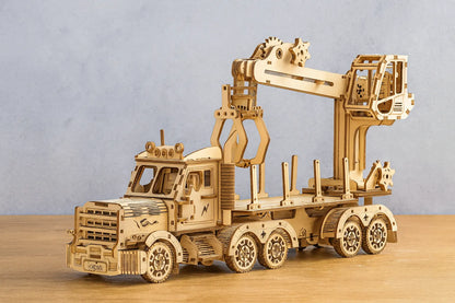 Maquette en bois d’un camion grue articulé posée sur une table en bois devant un mur gris clair.