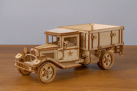 Maquette en bois d’un camion vintage décoré d’une étoile sur la portière, posée sur une table en bois devant un mur gris clair.