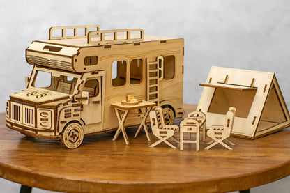 Maquette en bois d’un camping-car accompagnée d’une tente triangulaire et de mobilier de pique-nique, installée sur une table en bois devant un mur gris clair.