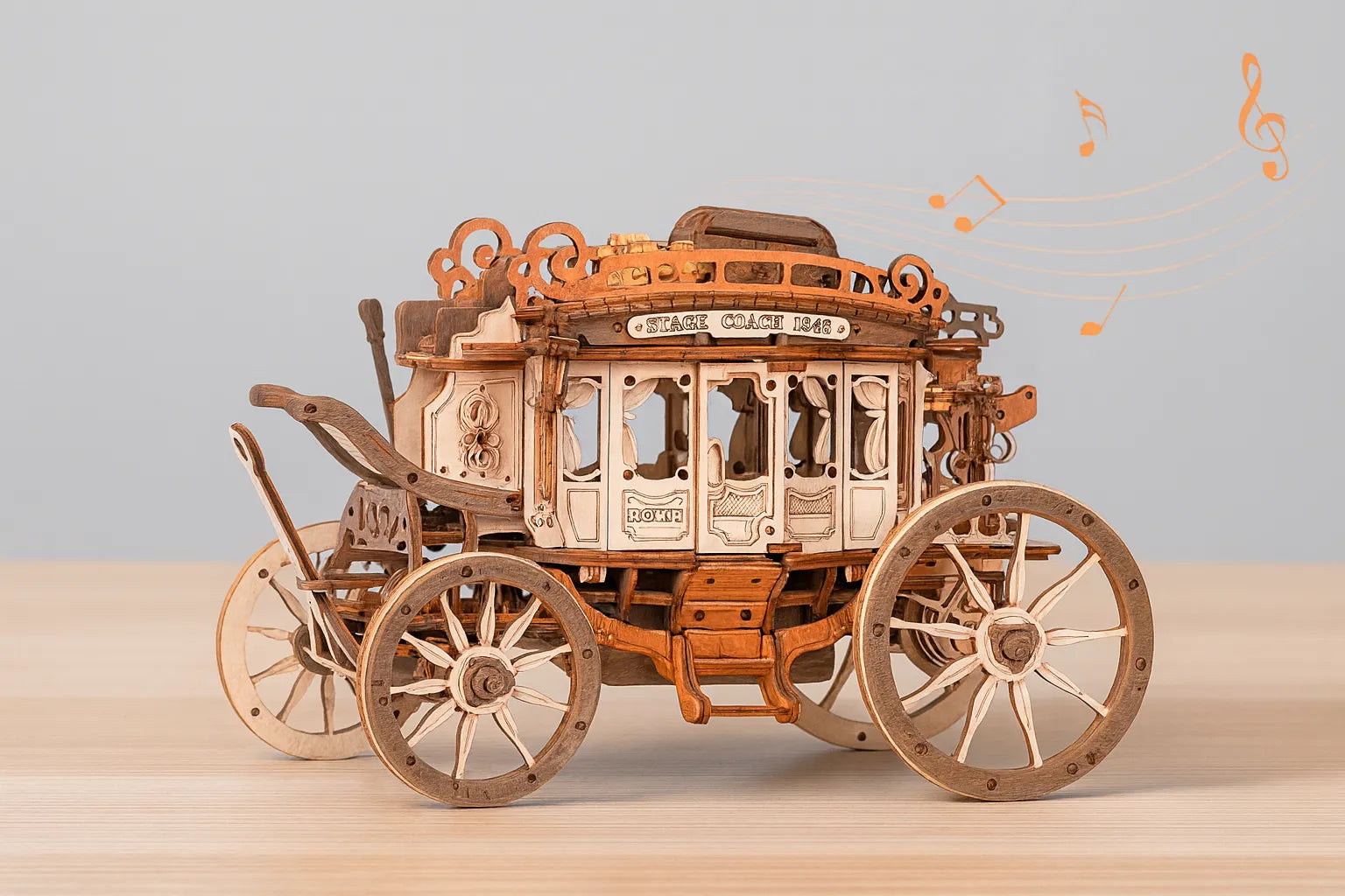 Maquette en bois d’un carrosse musical richement décoré, avec des notes de musique flottant autour, posée sur une table en bois devant un mur gris clair.