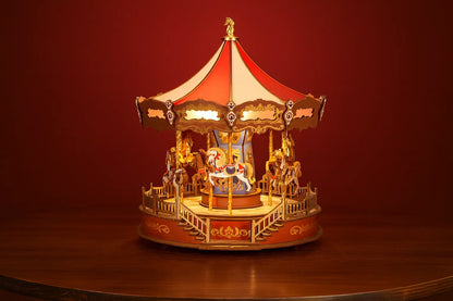 Maquette en bois d’un carrousel coloré avec chevaux posée sur une table en bois devant un mur rouge.