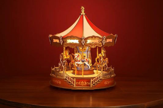 Maquette en bois d’un carrousel coloré avec chevaux posée sur une table en bois devant un mur rouge.