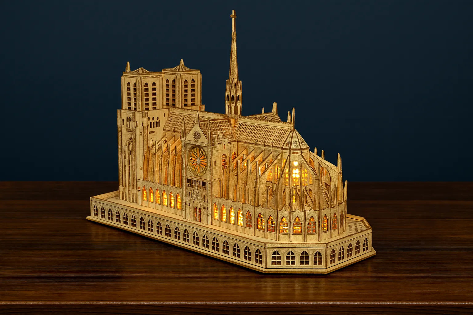 Maquette en bois illuminée de la cathédrale Notre-Dame de Paris, posée sur une table en bois devant un fond bleu foncé.