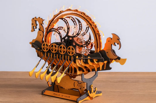 Maquette en bois d’un drakkar mécanique lumineux posé sur une table en bois devant un mur gris clair.