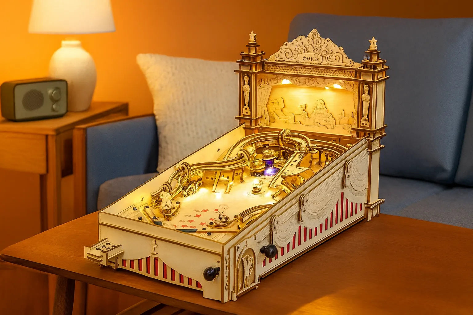 Maquette en bois d’un flipper rétro avec décorations sculptées et lumières intégrées, posée sur une table dans un salon à l’éclairage chaud et à la décoration vintage.