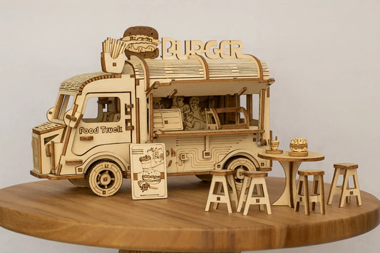 Maquette en bois d’un food truck en forme de camion de burgers avec tables et tabourets, placée sur une table en bois devant un mur gris clair.