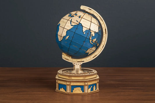 Maquette en bois d’un globe terrestre coloré bleu et beige posée sur une table en bois foncé et devant un mur gris.
