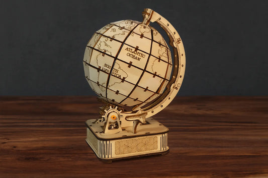 Maquette en bois d’un globe terrestre naturel clair posée sur une table en bois foncé et devant un mur gris.
