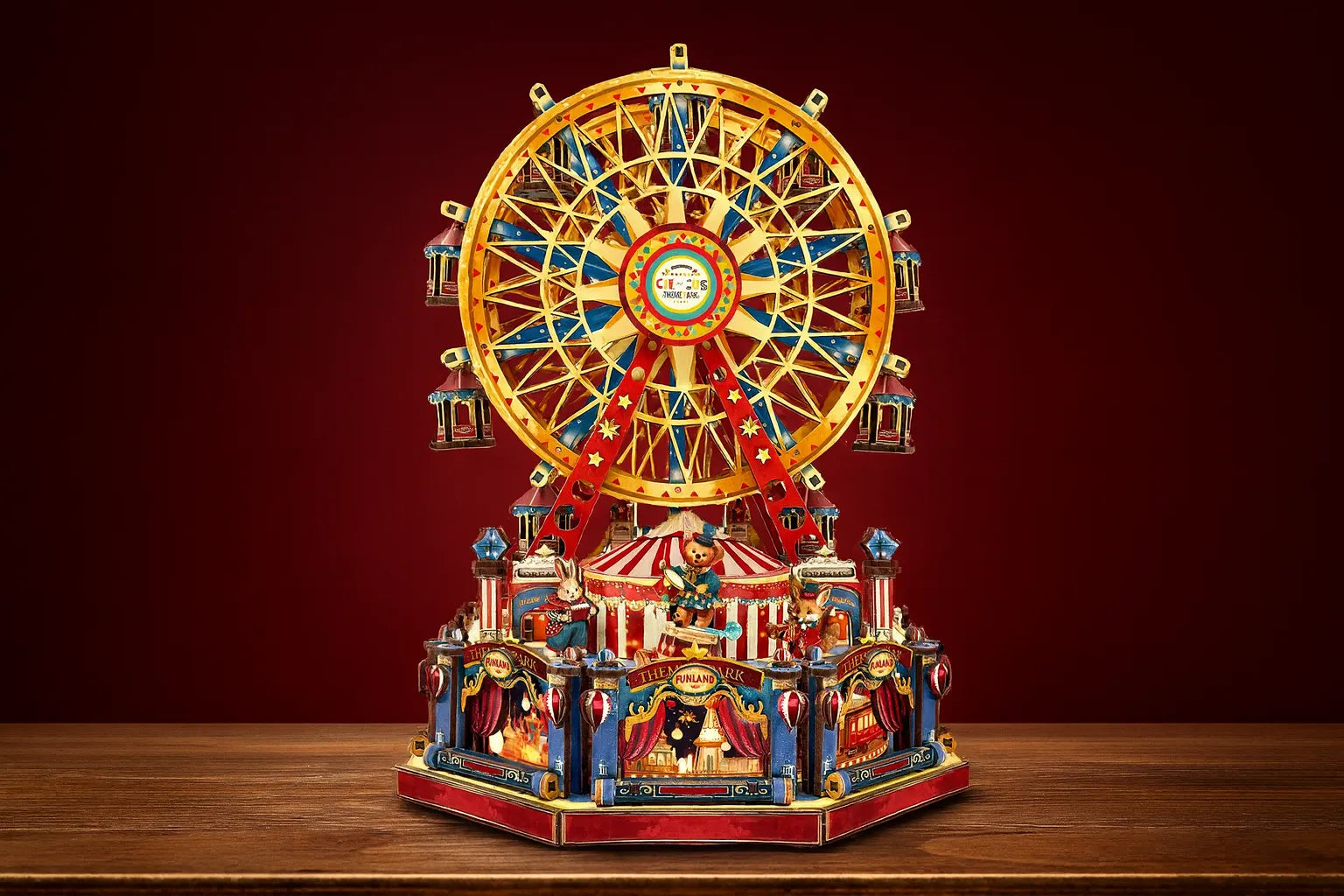 Maquette en bois d’une grande roue colorée posée sur une table en bois devant un mur rouge.