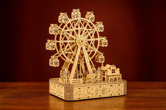 Maquette en bois d’une grande roue lumineuse posée sur une table en bois devant un mur rouge.