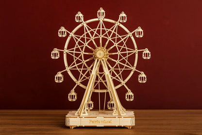 Maquette en bois d’une grande roue posée sur une table en bois devant un mur rouge.