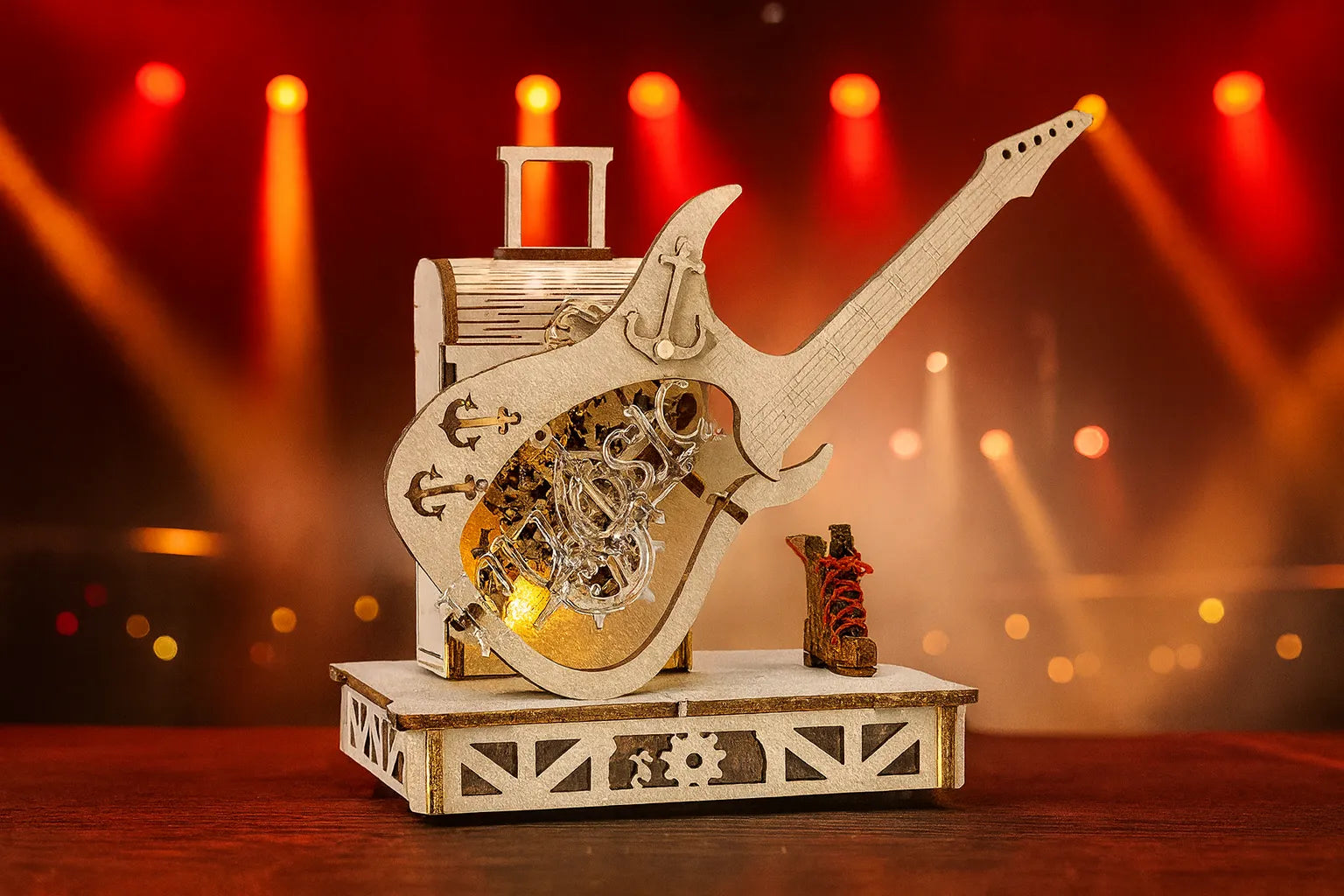 Maquette en bois d’une guitare électrique montée sur une boîte à musique, éclairée par des projecteurs de scène rouges et orangés.