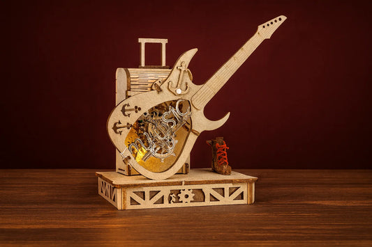 Maquette en bois d’une guitare électrique avec boîte à musique, posée sur une table en bois devant un fond rouge foncé.