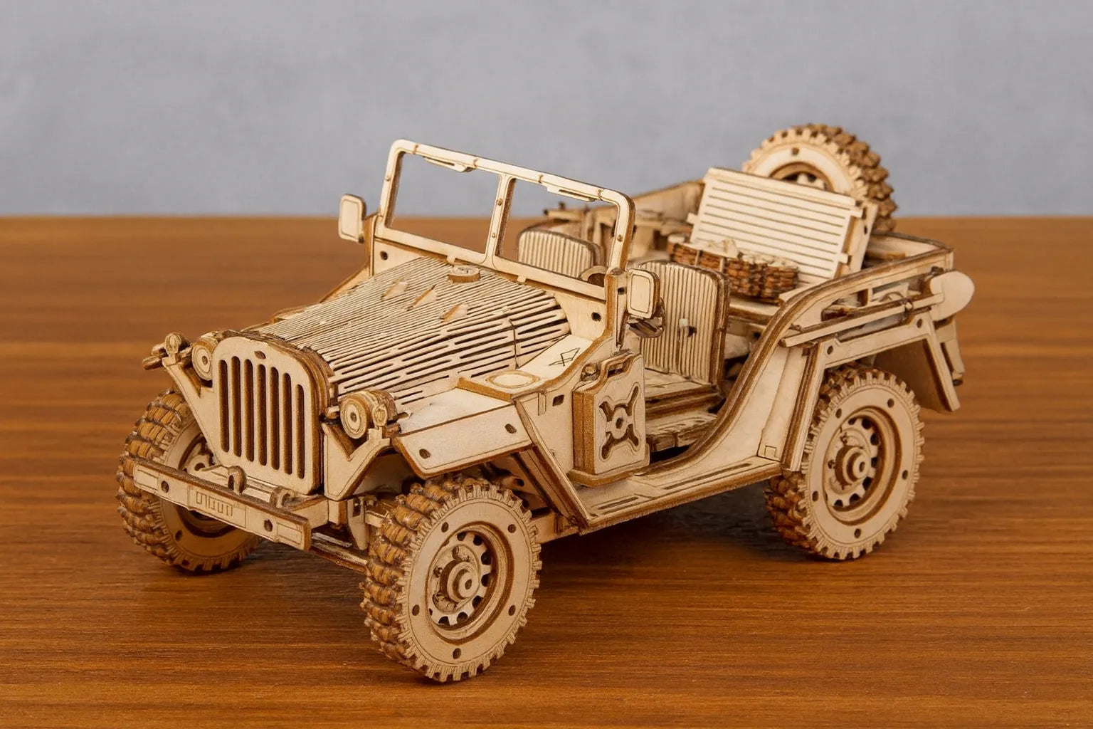 Maquette en bois d’une jeep militaire ouverte posée sur une table en bois devant un mur gris clair.