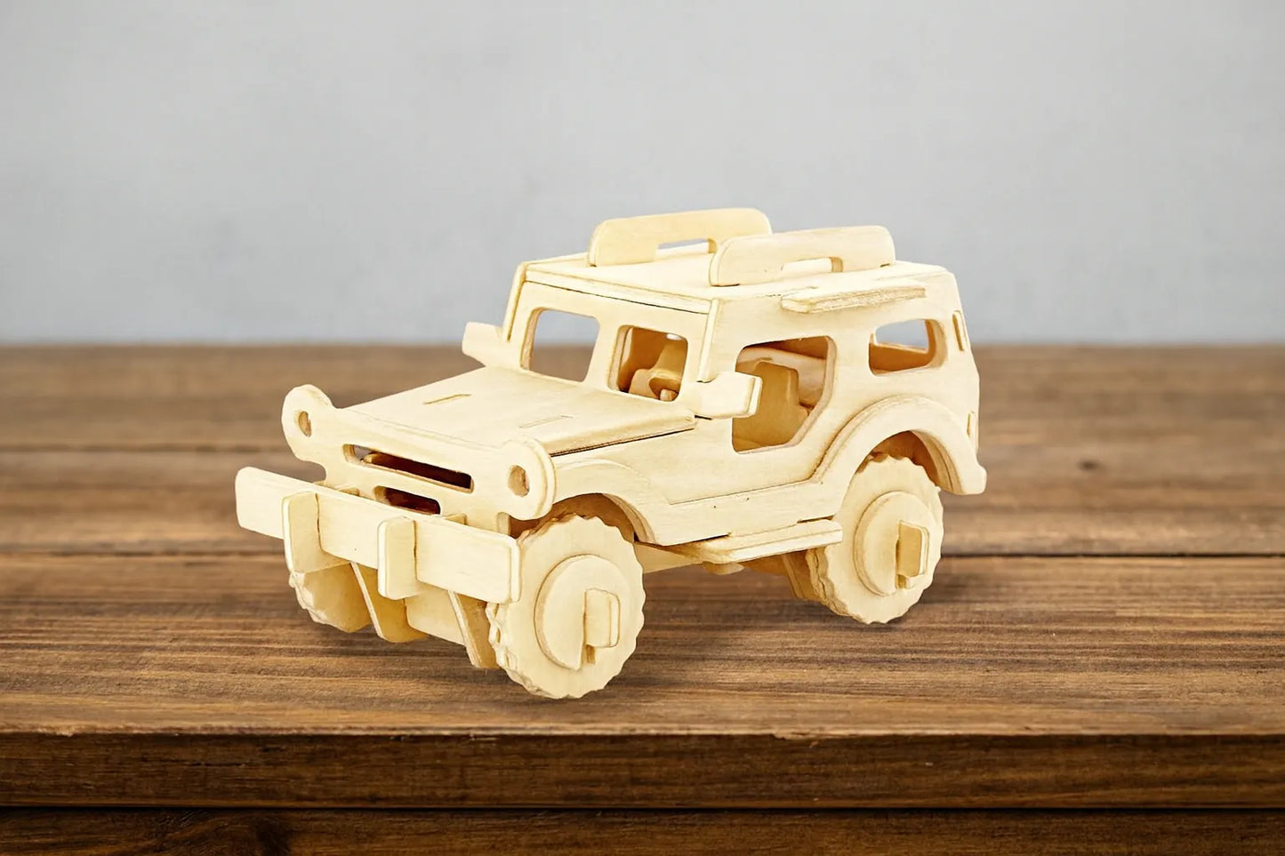 Maquette en bois d’une jeep tout-terrain beige, posée sur une table en bois devant un mur gris clair.