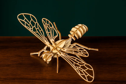 Maquette en bois d’une abeille posée sur une table en bois, ailes ouvertes devant un fond vert.