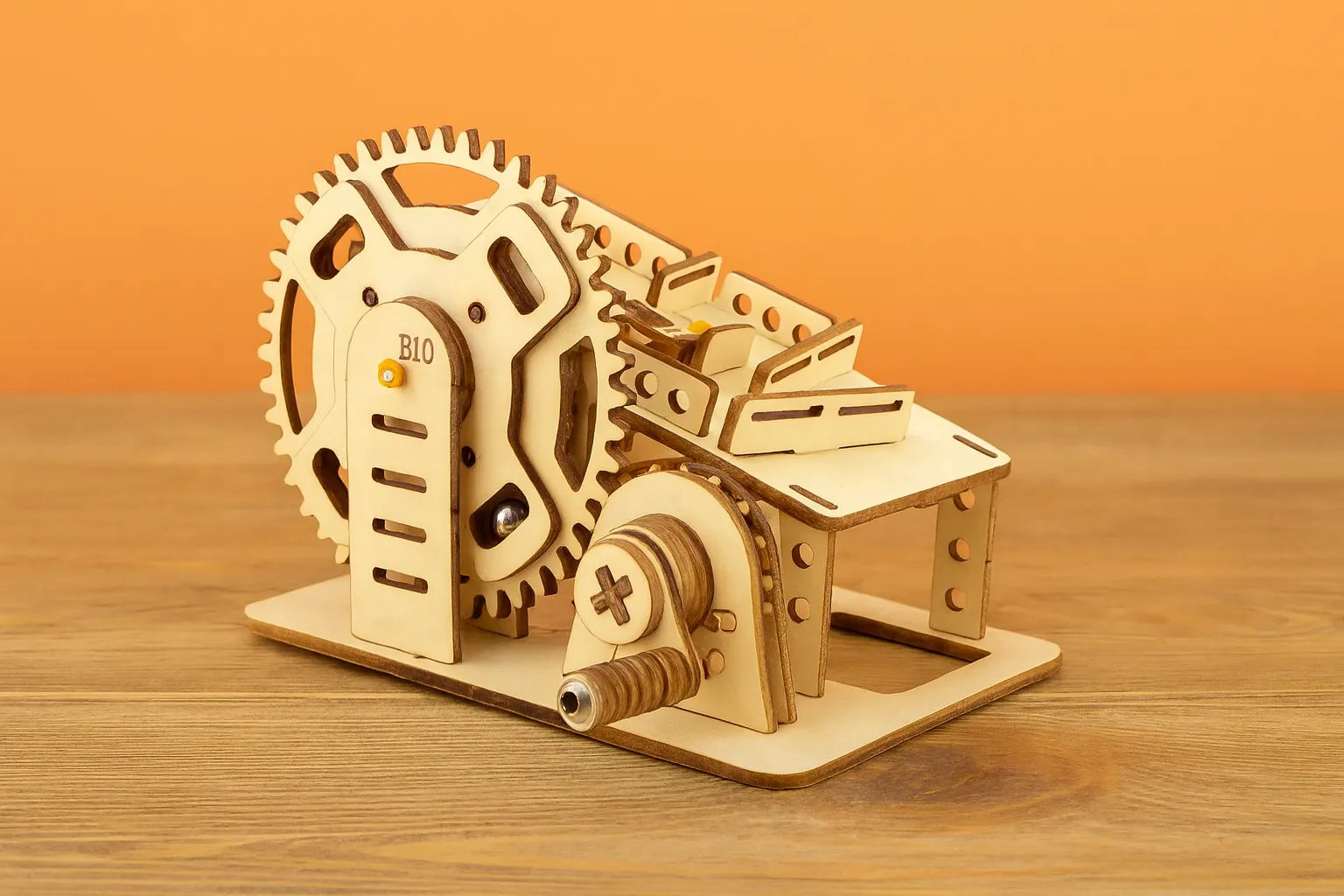 Maquette en bois d’un petit circuit de billes, composée d’engrenages et de rampes, posée sur une table en bois devant un mur orangé.