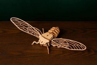 Maquette en bois d’une cigale posée sur une table en bois, vue du dessus, ailes déployées.