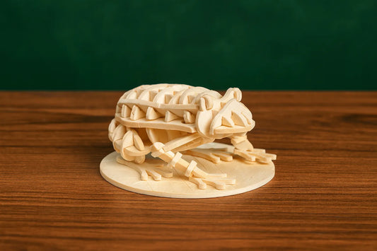 Maquette en bois d’une grenouille, posée sur une table en bois devant un fond vert foncé.