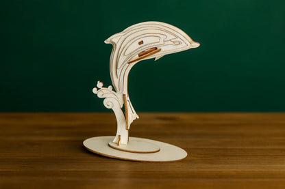 Maquette en bois d’un dauphin sur un socle ovale, présentée sur une table en bois avec un fond vert.