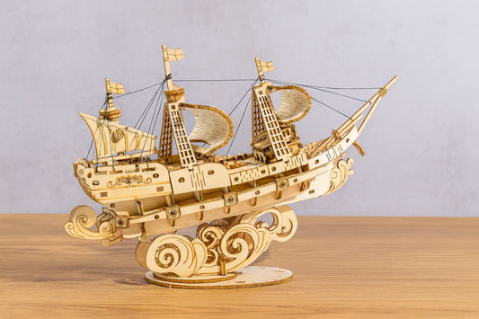 Maquette en bois d’un galion détaillé aux voiles courbées posée sur une table en bois devant un mur gris clair.