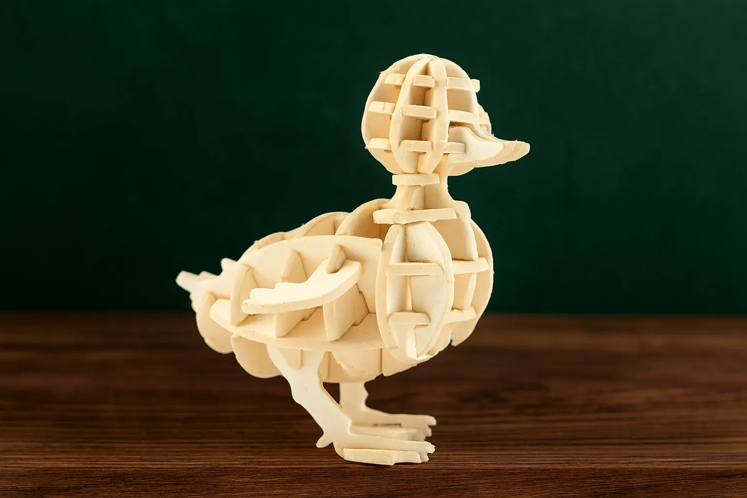 Maquette en bois d’un petit canard exposée sur une table en bois avec un fond vert foncé.