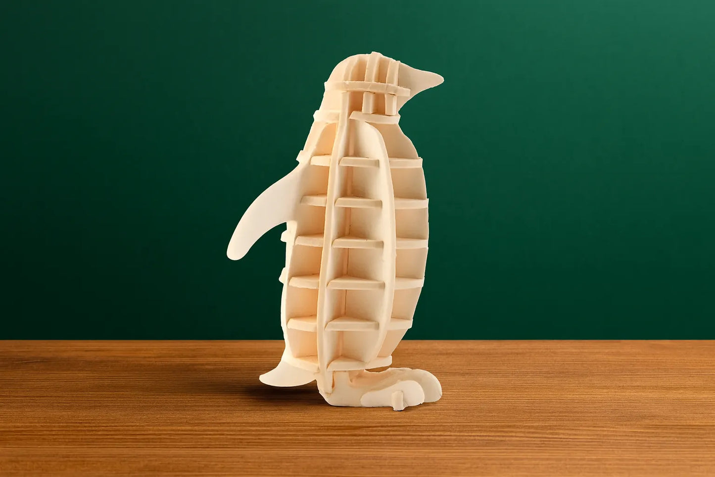 Maquette en bois représentant un manchot, placée sur une table en bois devant un fond vert foncé.