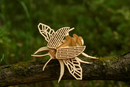 Maquette en bois d’un scarabée posée sur une branche recouverte de mousse, fond vert naturel.