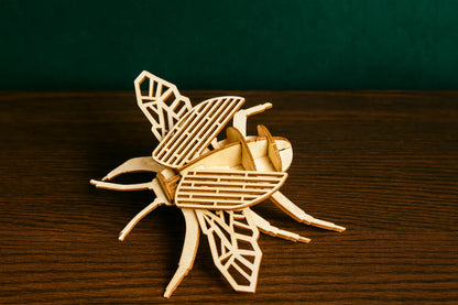 Maquette en bois d’un scarabée posée sur une table en bois, fond vert foncé.