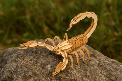 Maquette en bois de scorpion placée sur une pierre en extérieur, dans un environnement naturel.