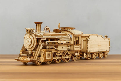 Maquette en bois d’une locomotive à vapeur avec tender posée sur une table en bois devant un mur gris clair.