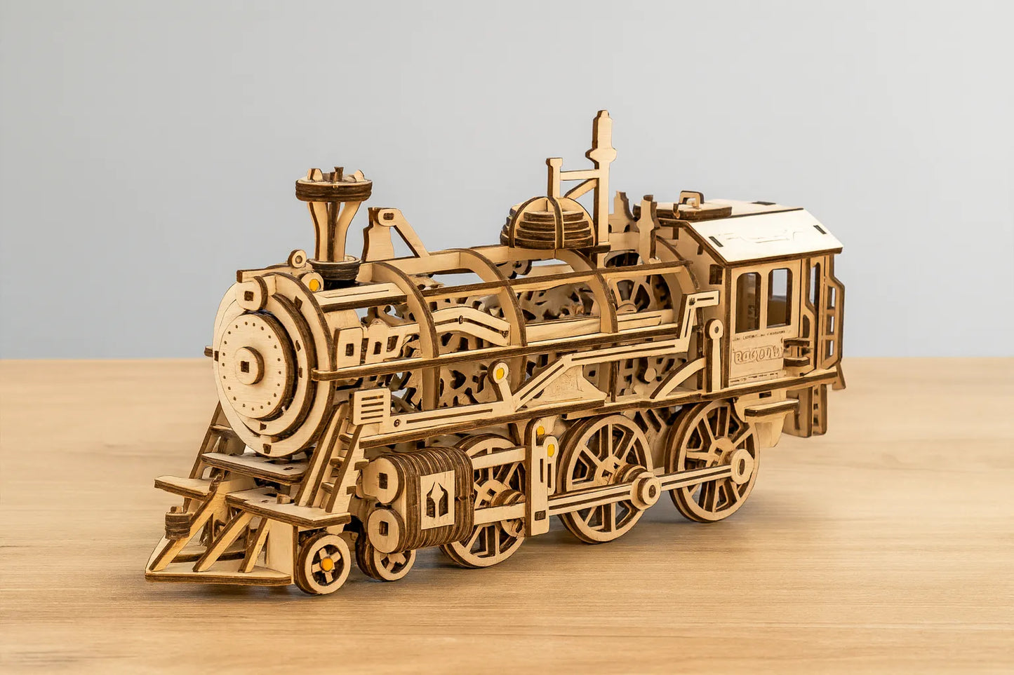 Maquette en bois d’une locomotive classique détaillée posée sur une table en bois devant un mur gris clair.
