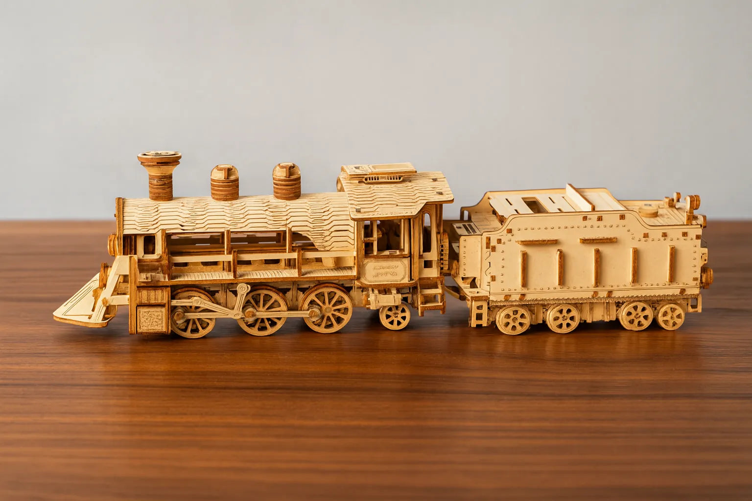 Maquette en bois d’une locomotive vintage détaillée avec tender, placée sur une table en bois devant un mur gris clair.