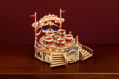 Maquette en bois d’un manège de tasses tournantes colorées posée sur une table en bois devant un mur rouge.