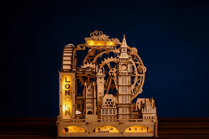 Maquette en bois illuminée représentant les monuments emblématiques de Londres, posée sur une table en bois devant un fond bleu foncé.