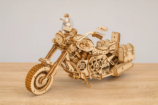 Maquette en bois d’une moto classique de type cruiser, dotée de nombreuses pièces mécaniques, posée sur une table en bois devant un mur gris clair.
