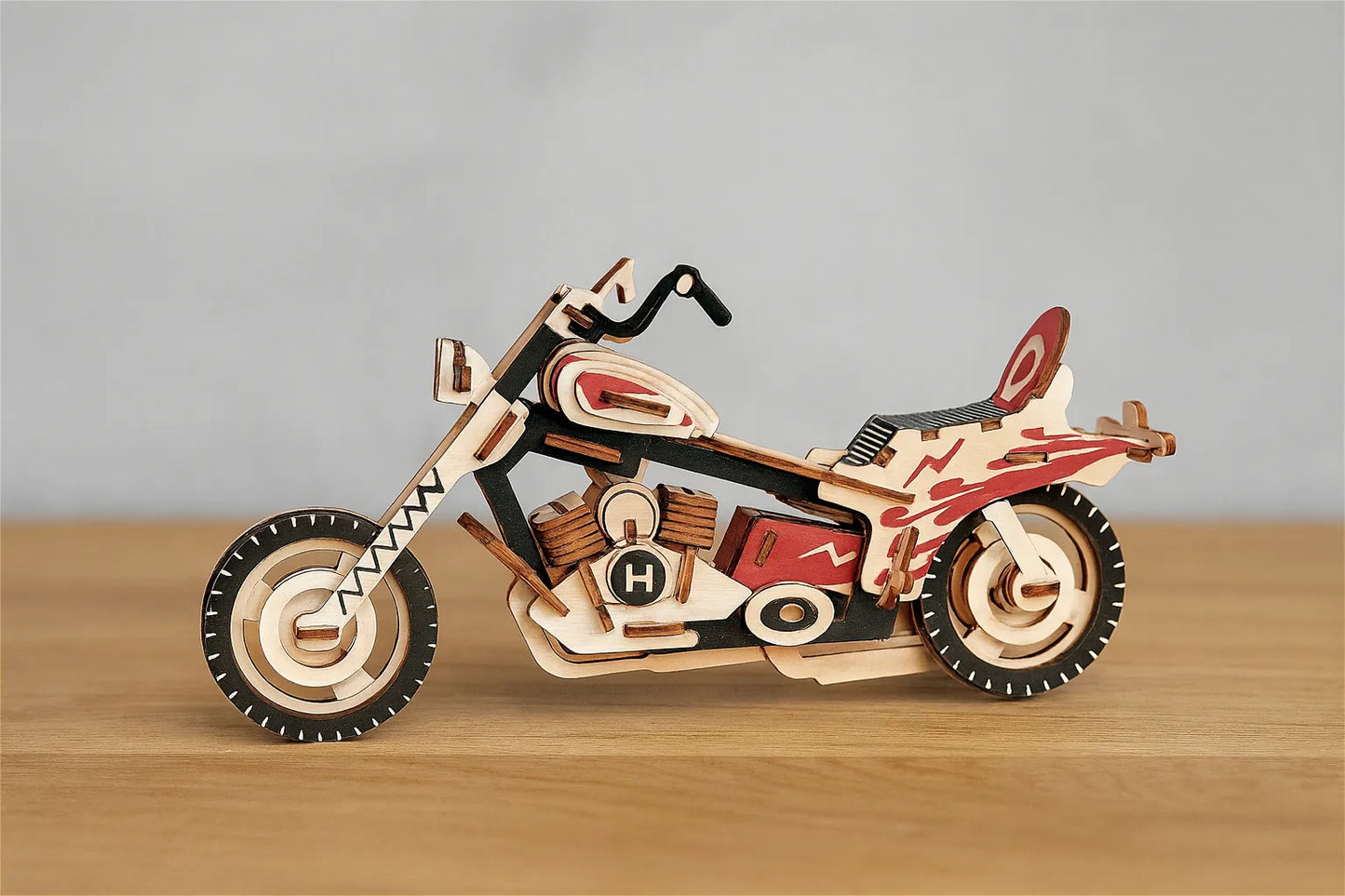 Maquette en bois d’une moto colorée rouge et noire posée sur une table en bois devant un mur gris clair.