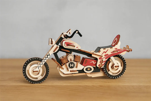 Maquette en bois d’une moto colorée rouge et noire posée sur une table en bois devant un mur gris clair.