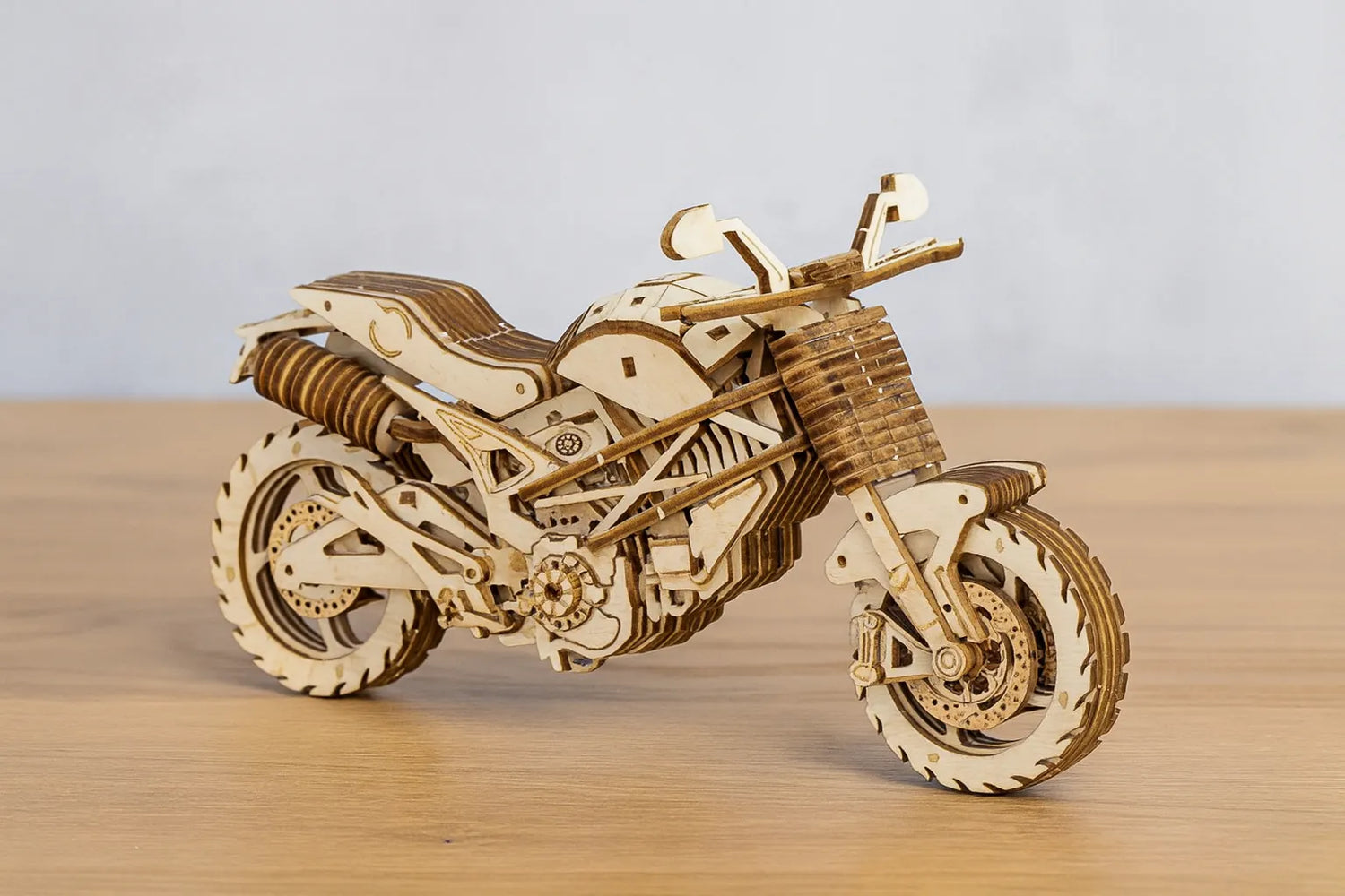 Maquette en bois d’une moto routière posée sur une table en bois devant un mur gris clair.