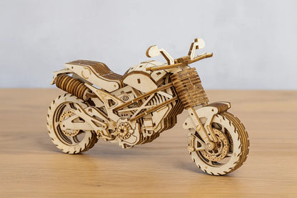 Maquette en bois d’une moto routière posée sur une table en bois devant un mur gris clair.