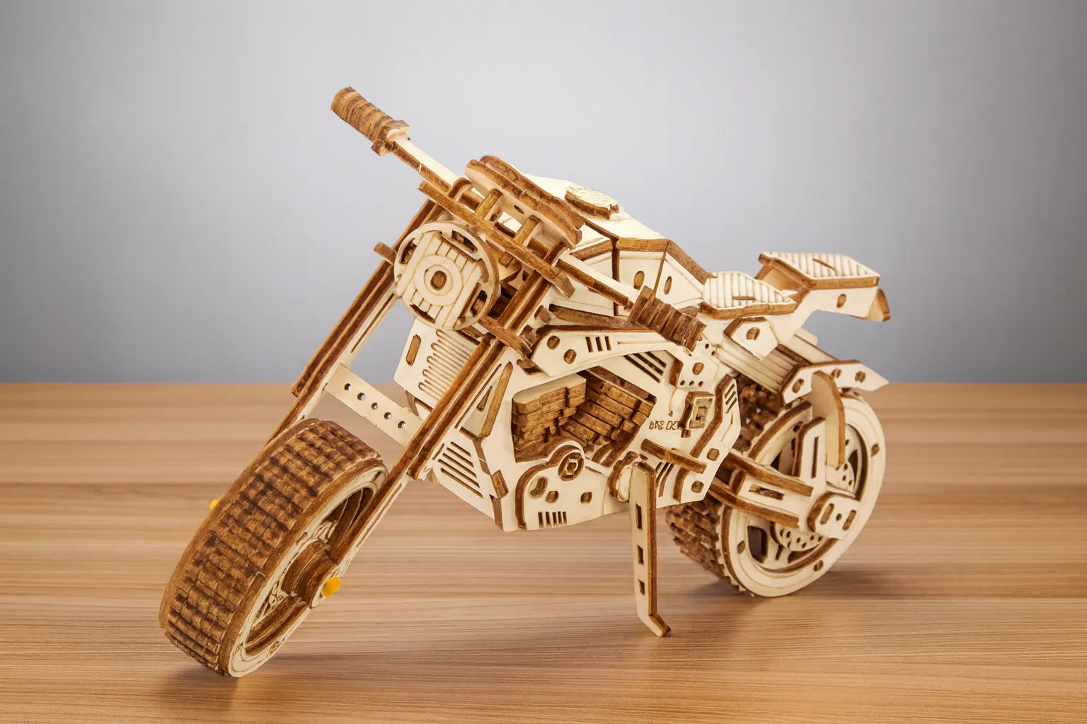 Maquette en bois d’une moto sportive, au design anguleux et mécanique, posée sur une table en bois devant un mur gris clair.